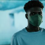 A young man in a mask stands in front of a blurred background, illustrating air pollution and safety.