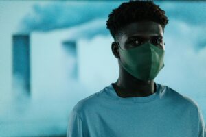 A young man in a mask stands in front of a blurred background, illustrating air pollution and safety.