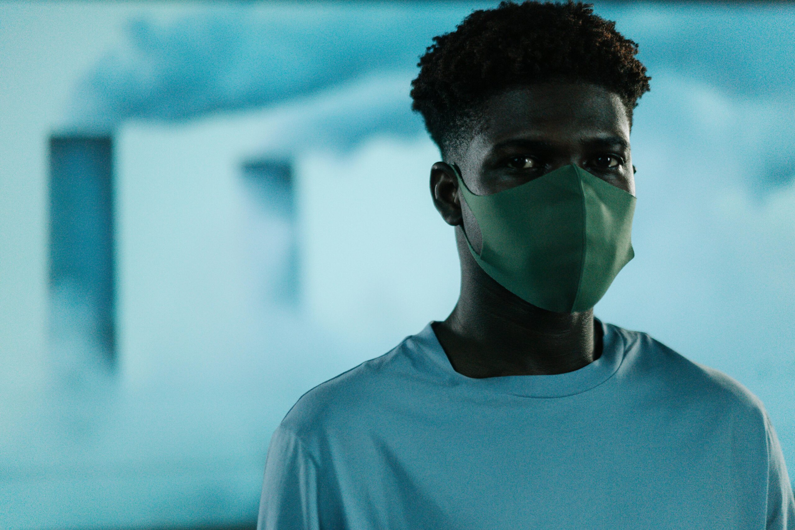 A young man in a mask stands in front of a blurred background, illustrating air pollution and safety.